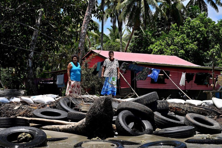 Esta fotografía tomada el 13 de diciembre de 2022 muestra a la residente Lavenia McGoon (derecha) con un miembro de su familia frente a un malecón improvisado con llantas de goma viejas para evitar la erosión, afuera de su casa frente a la playa en un pueblo de la ciudad costera de Togoru, a unos 35 kilómetros. de la capital de Fiji, Suva.&nbsp;&nbsp;