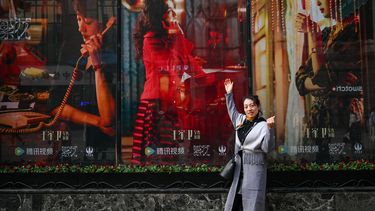 La foto tomada el 7 de enero de 2024 muestra a una mujer posando junto a los carteles de la serie de televisión china Blossoms Shanghai, dirigida por el cineasta hongkonés Wong Kar-wai, en Shanghai.