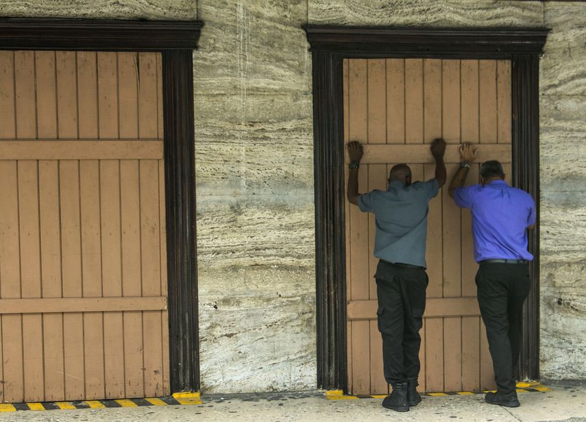 Unas personas cubren con madera la fachada de una farmacia mientras se preparan para la llegada de la tormenta tropical Dorian, en Bridgetown, Barbados, el lunes 26 de agosto de 2019.&nbsp;