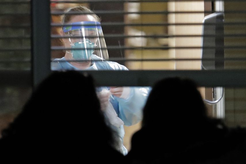 Una trabajadora vestida con una máscara y un traje de protección, vista a través de una ventana en el interior de la habitación de Susan Hailey, de 76 años, quien dio positivo por un nuevo coronavirus, mientras las hijas de la paciente observan desde fuera, el 10 de marzo de 2020, en el Life Care Center en Kirkland, Washington, cerca de Seattle, EEUU. 