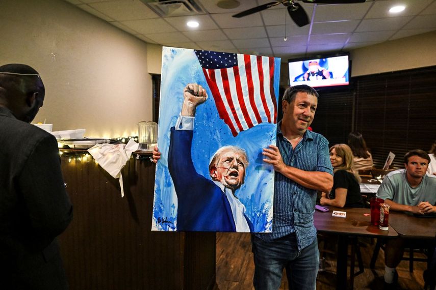 Un hispano levanta una pintura alegórica al momento en que Trump sube su brazo en señal de victoria tras el atentado en Pennsylvania.