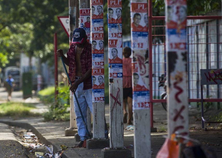 Un hombre barre una acera frente a postes con propaganda política en una calle de Managua el 3 de noviembre de 2017, durante el inicio del silencio electoral previo a los comicios.