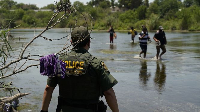 Inmigrantes cruzan el Río Bravo ante la mirada de un agente de Inmigración.