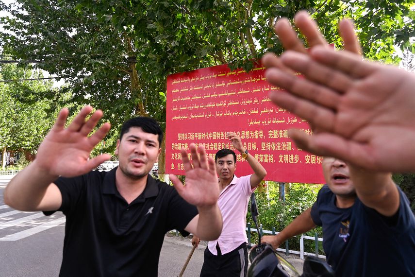 Esta fotografía tomada el 18 de julio de 2023 muestra a hombres locales tratando de impedir que se tome una fotografía de un cartel con propaganda política en la aldea de Azatbagh, en las afueras de Yarkant, en la región de Xinjiang, en el noroeste de China.&nbsp; &nbsp;