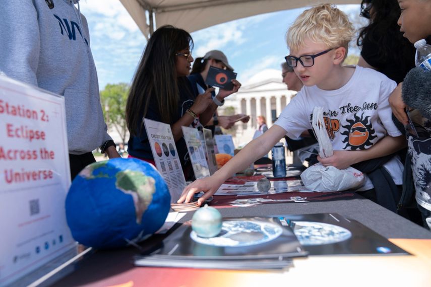 Los niños navegan por el puesto de información de la NASA mientras se reúnen para observar cómo la luna cubre parcialmente el sol durante un eclipse solar total en Washington, el lunes 8 de abril de 2024.