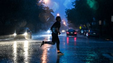 Un hombre cruza la calle durante fuertes lluvias y vientos que afectan la Florida.