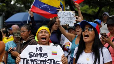 En Venezuela, una mujer sostiene un cartel con un mensaje que dice en español; No somos terroristas, mientras espera con sus compañeros la llegada de la líder opositora María Corina Machado, tras elecciones.