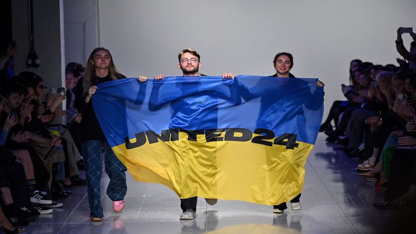 Los diseñadores de moda ucranianos Ksenia Schnaider, Ivan Frolov y Julie Paskal ondean la bandera de Ucrania mientras caminan por la pasarela antes de la colección de desfiles de moda ucranianos Otoño/Invierno 2023 en el 5to día de la Semana de la Moda de Londres el 21 de febrero de 2023.