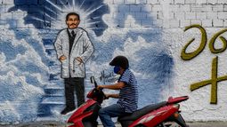 Un hombre con mascarillas pasa su motocicleta frente a un mural que representa al médico venezolano José Gregorio Hernández en una calle de Caracas, el 27 de abril de 2021. La Iglesia católica beatificará al médico venezolano José Gregorio Hernández el 30 de abril en Caracas.