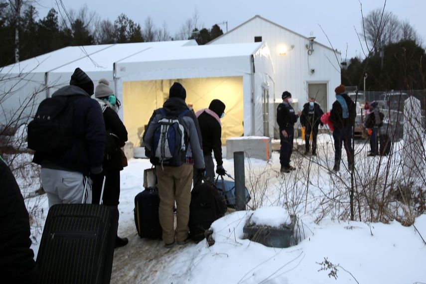 Migrantes hacen una fila en la frontera entre Estados Unidos y Canadá, en un centro de recepción para personas que cruzan a territorio canadiense sin autoridad legal, en Saint-Bernard-de-Lacolle, Quebec, Canadá, el miércoles 12 de enero de 2022, en una fotografía tomada desde Champlain, Nueva York.