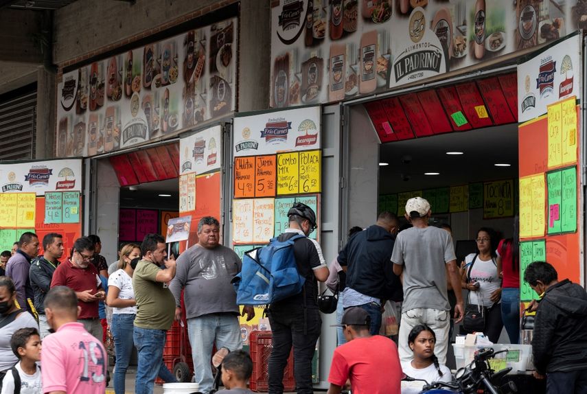 Un grupo de personas hace fila para comprar salchichas y queso en una tienda cerca del mercado municipal de Quinta Crespo que muestra los precios en dólares en Caracas, Venezuela.