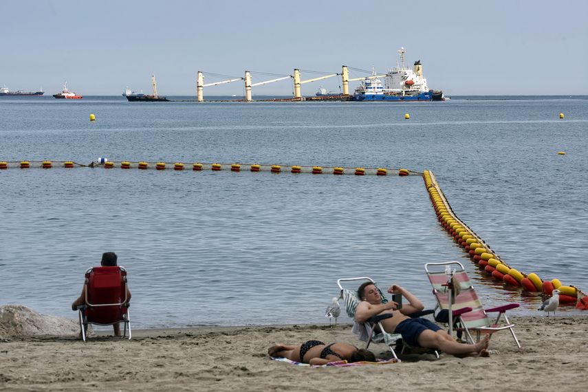 Personas descansando el jueves 1 de septiembre de 2022 en una playa frente al buque de carga OS 35, que chocó con un buque de gas natural líquido en la bahía de Gibraltar el lunes pasado.&nbsp;