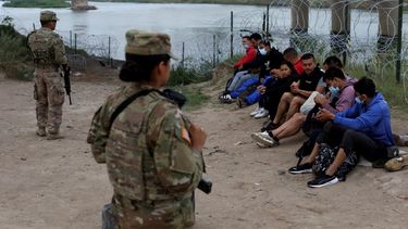 Varios migrantes que cruzaron el río Bravo hacia Estados Unidos bajo la custodia de miembros de la Guardia Nacional mientras esperan la llegada de agentes de la Patrulla Fronteriza en Eagle Pass, Texas, el viernes 20 de mayo de 2022.&nbsp;