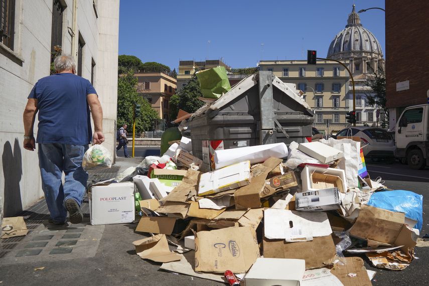 Un hombre pasa junto a una pila de basura con la cúpula de la basílica de San Pedro del Vaticano al fondo, en Roma, el 24 de junio de 2019. 