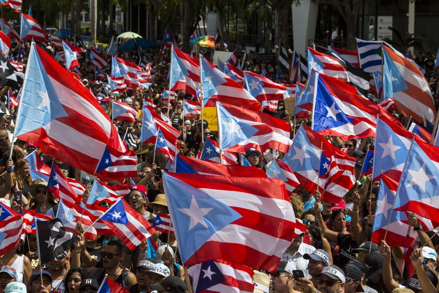 Personas desfilan ondeando la bandera de Puerto Rico para celebrar la renuncia del gobernador Ricardo Rosselló, quien anunció que dejará el cargo el 2 de agosto después de varias semanas de manifestaciones debido a la filtración de un chat repleto de obsenidades e insultos misóginos, el jueves 25 de julio de 2019, en San Juan.&nbsp;