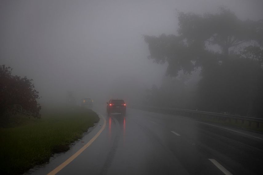 Un automóvil atraviesa una densa niebla y lluvias.