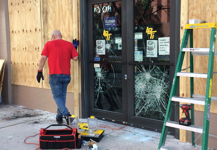 Un hombre repara la fachada de un local comercial en el centro de Miami, tras sufrir da&ntilde;os la noche del s&aacute;bado 30 d emayo.