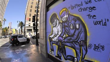 Un mural dibujado en los tablones que protegen un negocio mientras una patrulla del Departamento de Polic&iacute;a de Los &Aacute;ngeles pasa por el lugar, el martes 9 de junio de 2020, en la secci&oacute;n de Hollywood, en Los &Aacute;ngeles.