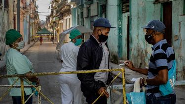 Un residente muestra su identificación a un oficial de policía que está limitando el acceso a un vecindario como una forma de frenar la propagación de la pandemia de COVID-19, mientras enfermeras están detrás en La Habana, Cuba.