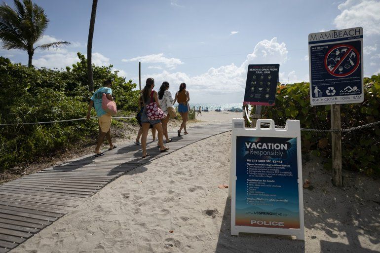 La gente pasa por un centro de letreros sobre las reglas de Miami Beach en la playa, en South Beach, Florida, el 9 de mayo de 2021.  
