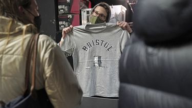 Una persona dentro de Rough Trade en Bristol, Inglaterra, sábado 11 de diciembre de 2021, muestra una camiseta diseñada por el artista callejero Banksy, en venta para apoyar a cuatro personas juzgadas por daños criminales por estar implicadas en derribar la estatua del comerciante de esclavos Edward Colston.