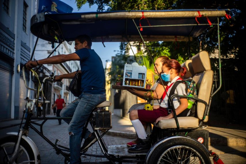 Una niña viaja a la escuela acompañada de su madre cargando su trabajo escolar en un bicitaxi en La Habana, Cuba.
