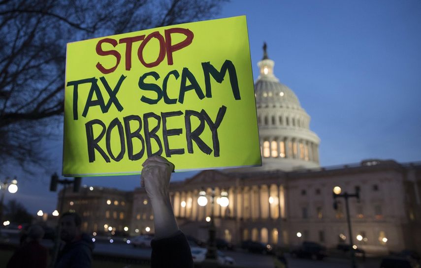 Un hombre sostiene un cartel en el que se lee: Paren la estafa del robo de&nbsp;impuestos, afuera del edificio del Capitolio de los Estados Unidos, este 30 de noviembre de 2017.