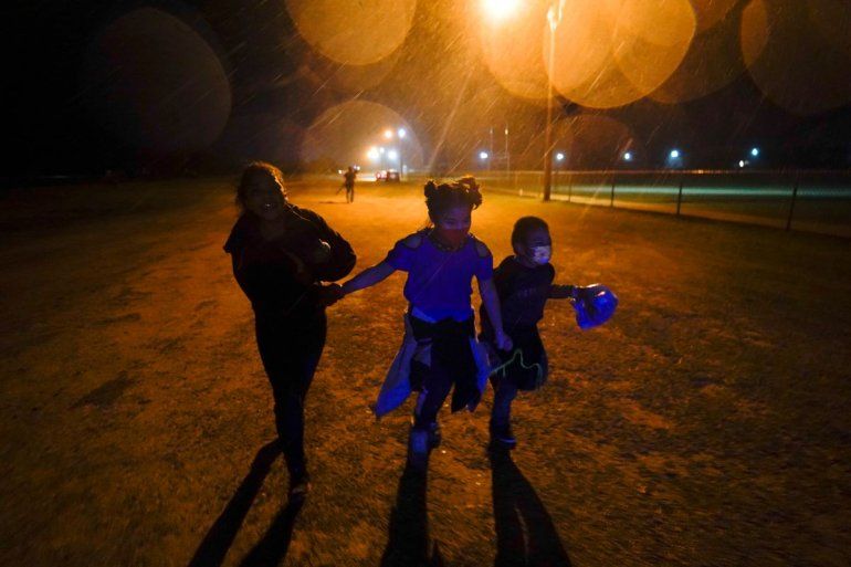 Tres migrantes se toman de las manos mientras corren bajo la lluvia en una zona de detención después de entregarse a las autoridades luego de cruzar la frontera desde México hacia Estados Unidos en Roma, Texas.