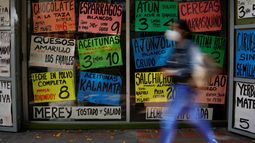 Una mujer camina frente a carteles que muestran los precios de los productos en dólares estadounidenses, frente a una tienda de comestibles en Caracas, Venezuela, el martes 18 de enero de 2022.