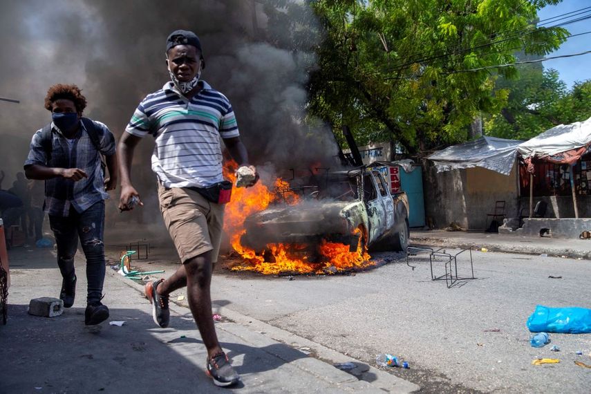 Unas personas se alejan de un autom&oacute;vil en llamas durante una protesta el lunes 5 de octubre de 2020 en Puerto Pr&iacute;ncipe, para exigir justicia por la muerte de un manifestante que fue baleado por la polic&iacute;a la semana pasada.
