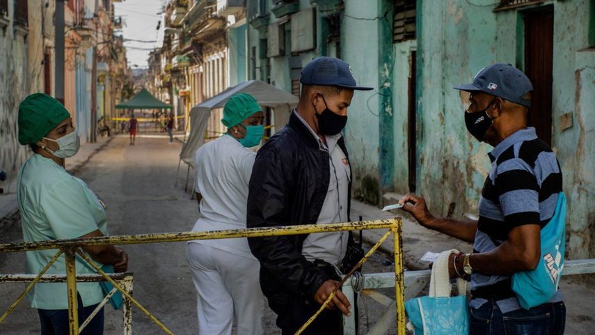 Un residente muestra su identificación a un oficial de policía que está limitando el acceso a un vecindario como una forma de frenar la propagación de la pandemia de COVID-19, mientras enfermeras están detrás en La Habana, Cuba.