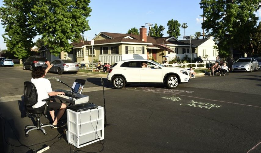 En esta fotograf&iacute;a del 9 de mayo de 2020 el m&uacute;sico Adam Chester, izquierda, saluda a un vecino que pasa en su auto mientras interpreta su concierto semanal en su barrio en la secci&oacute;n de Sherman Oaks en Los Angeles. Chester suele ser un sustituto de Elton John, canta y coca en los ensayos del super astro.&nbsp;