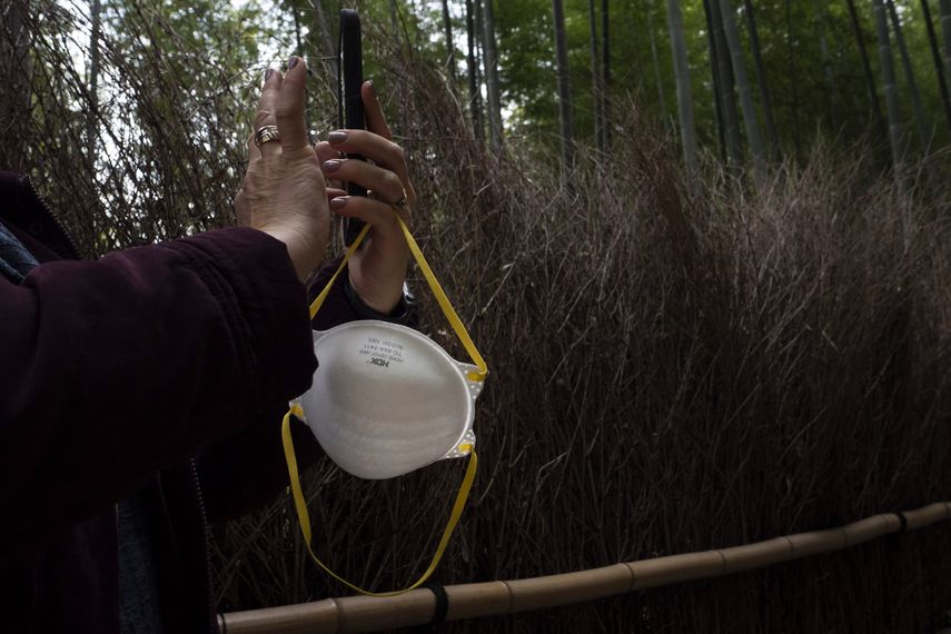 Una turista sostiene una mascarilla mientras hace fotos en el bosque de bamb&uacute; de Arashiyama en Kioto, Jap&oacute;n, el 18 de marzo de 2020.&nbsp;