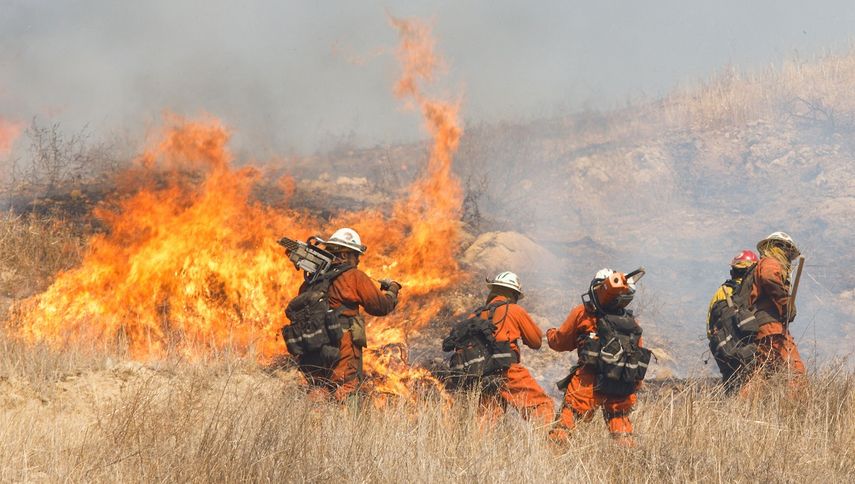 Los bomberos trabajan para extinguir un brote del incendio Woolsey en una colina en West Hills, California.