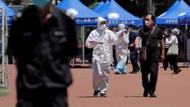   Un trabajador sanitario en traje de protección conversa con un hombre que ya sea vive en los alrededores del mercado mayorista de Xinfadi o lo visitó recientemente, para que se realice una prueba de ácido nucleico en las afueras de un estadio, en Pekín, el domingo 14 de junio de 2020.