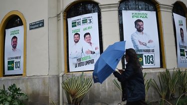 Una mujer camina con un paraguas junto a carteles de la campaña electoral de los candidatos a la cámara y al Senado de la Alianza Verde, Fabián Peña y Ariel Ávila, en Bogotá, el 3 de marzo de 2026. Colombia celebrará elecciones legislativas el 8 de marzo