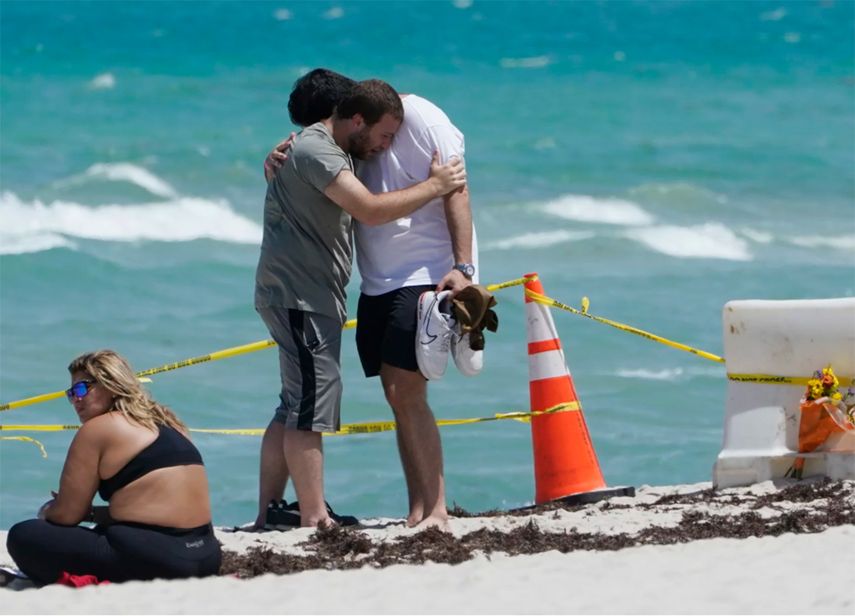 Dos jóvenes se abrazan y se consuelan, mientras una joven mira de reojo el derrumbe del edificio, en Surfise, al norte de Miami Beach.