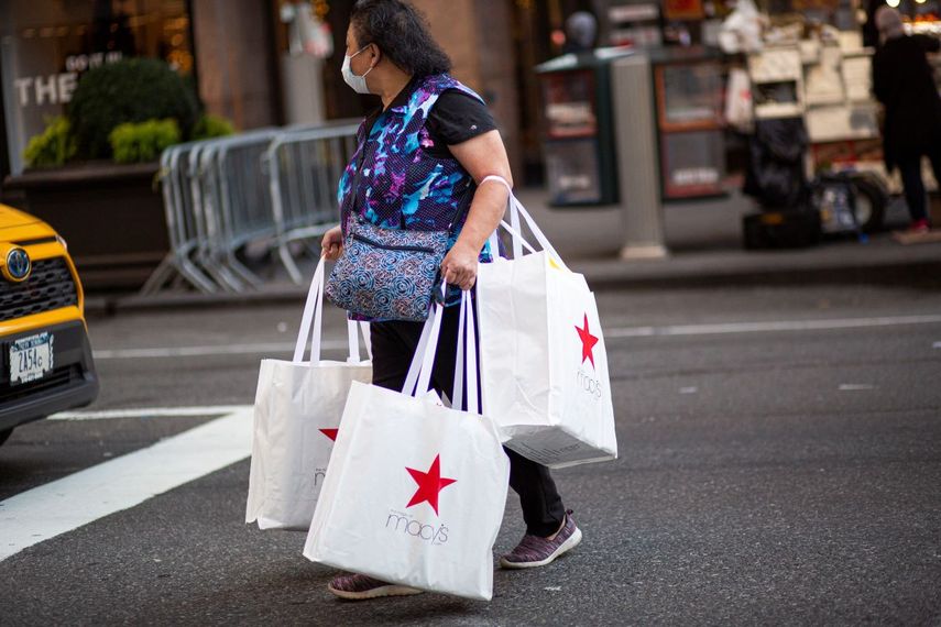 Una mujer que se protege con una mascarilla del COVID-19 sale de la tienda Macys con paquetes de compras
