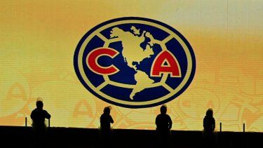 Siluetas de policías antidisturbios frente al jumbotrón que muestra el escudo del club de fútbol América antes del partido de fútbol Clausura de la Liga MX entre América y Cruz Azul en el Estadio de la Ciudad Deportiva en la Ciudad de México el 12 de abril de 2025.