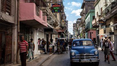 Varias personas caminan bajo el cartel que anuncia la existencia de una tienda de comestibles privada en La Habana, Cuba.