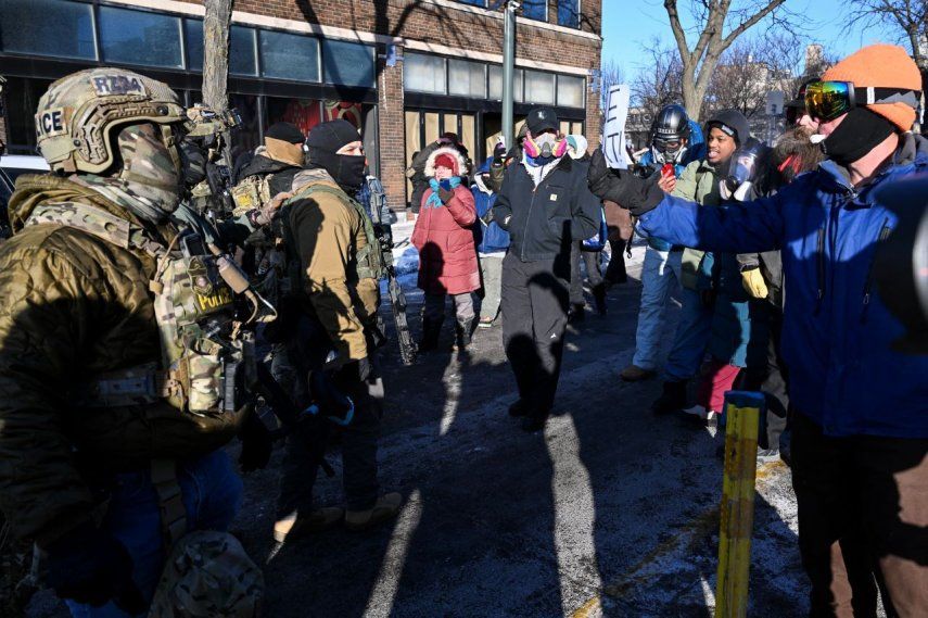 Agentes federales observan mientras los manifestantes se reúnen cerca del lugar donde las autoridades estatales y locales dicen que un hombre fue baleado por agentes federales más temprano esa mañana en Minneapolis, Minnesota, el 24 de enero de 2026.