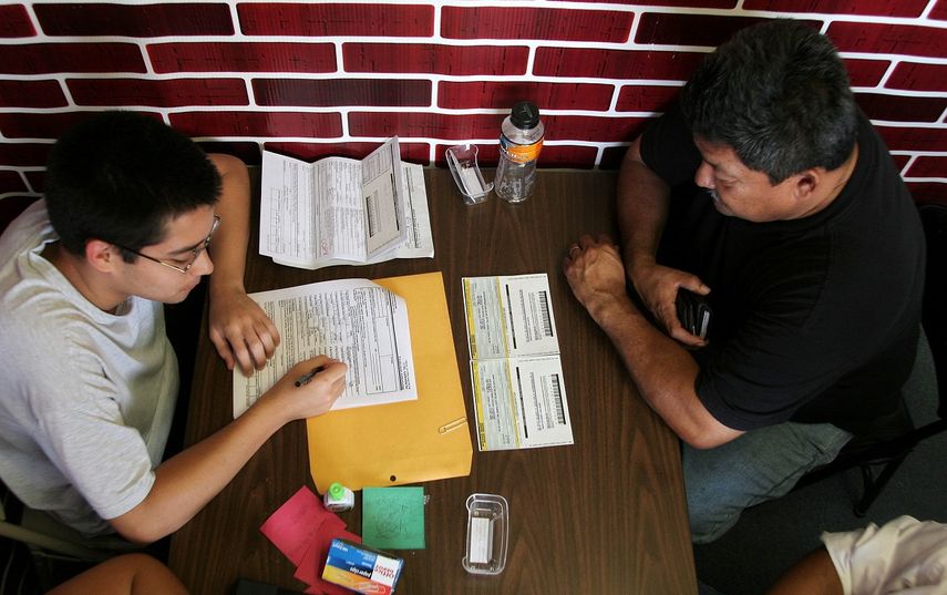 Fotografía de archivo que muestra a un joven hondureño asistiendo a un compatriota para rellenar los formularios de renovación del Estatuto de Protección Temporal, TPS.