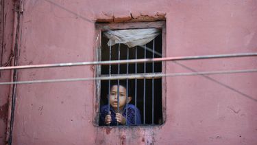 Un niño mira por la ventana de su casa en el barrio viejo de Nueva Delhi, India, 27 de marzo de 2020. Oxfan dijo el jueves 9 de abril de 2020 que el impacto económico de la pandemia de coronavirus podría arrojar a 500 millones de personas a la pobreza en el mundo. 