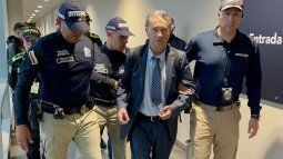 Esta fotografía, difundida por la Dirección Nacional de Migración y Extranjería de Colombia, muestra a agentes de migración y policías colombianos escoltando al excapo del Cártel de Medellín, Carlos Lehder Rivas (centro), a su llegada tras ser deportado desde Fráncfort al Aeropuerto Internacional El Dorado de Bogotá el 28 de marzo de 2025.&nbsp;