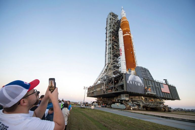 Los invitados y los empleados de la NASA toman fotos mientras el cohete del Sistema de Lanzamiento Espacial (SLS) de la NASA con la nave espacial Orion a bordo sale de High Bay 3 del edificio de ensamblaje de vehículos por primera vez, en el Centro Espacial Kennedy en Cabo Cañaveral, Florida.