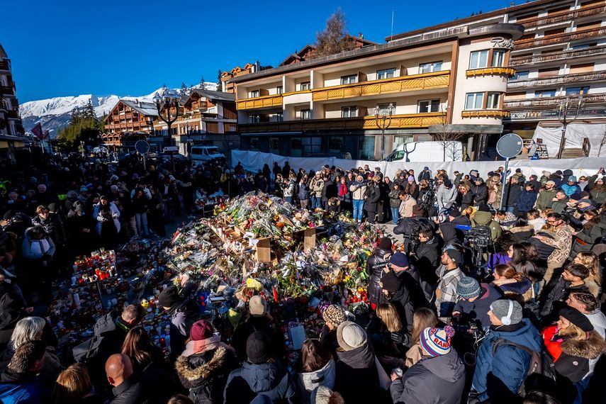 La gente se reúne alrededor de un monumento improvisado para presentar sus respetos depositando flores, velas y mensajes cerca del bar Constellation, el 4 de enero de 2026, en Crans-Montana, en honor a las víctimas del incendio que arrasó el local en la lujosa estación de esquí alpina la víspera de Año Nuevo. &nbsp;