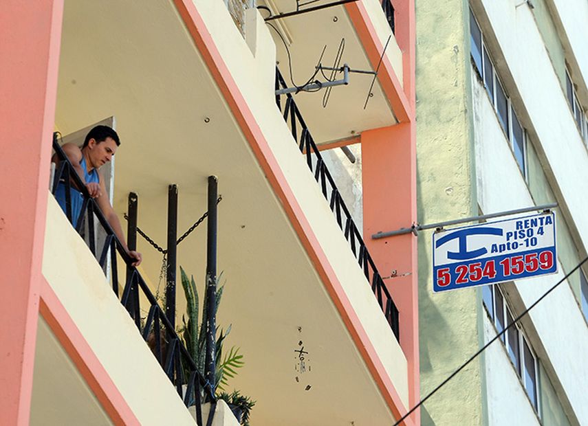 Un joven se asoma a su balcón junto a un cartel de renta de habitaciones en La Habana. (EFE)