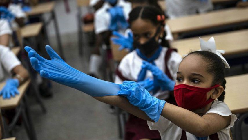 Una estudiante con máscara se pone guantes de plástico como medida de precaución en medio de la propagación del nuevo coronavirus durante una clase en La Habana, Cuba, el lunes 2 de noviembre de 2020. Decenas de miles de escolares regresaron a clases el lunes en La Habana por primera vez desde que la pandemia de coronavirus llevó a las autoridades a cerrar la isla en abril.
