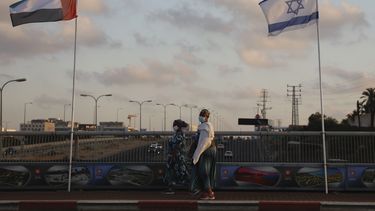 Mujeres con cubrebocas para evitar la propagaci&oacute;n del coronavirus pasan entre las banderas de los Emiratos &Aacute;rabes Unidos e Israel en el Puente de la Paz en Netanya, Israel, el domingo 16 de agosto de 2020. (AP Foto/Ariel Schalit)