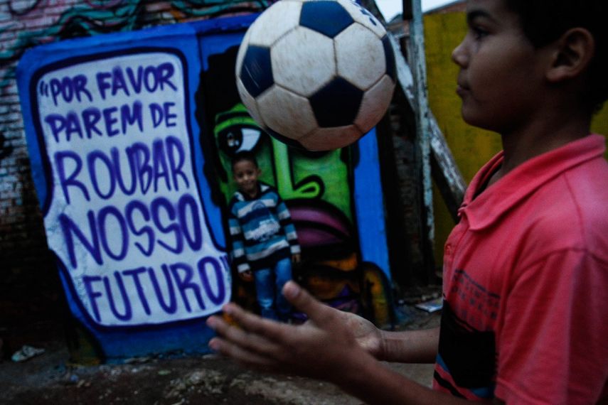 Dos niños juegan con un balón frente a un grafiti contra la corrupción y la impunidad en la política brasileña del artista y activista Mundano, en la favela del Moinho, en Sao Paulo, Brasil.&nbsp;